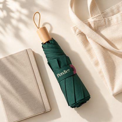 Folded wooden-handle umbrella with its snap band, beside a notebook and tote bag