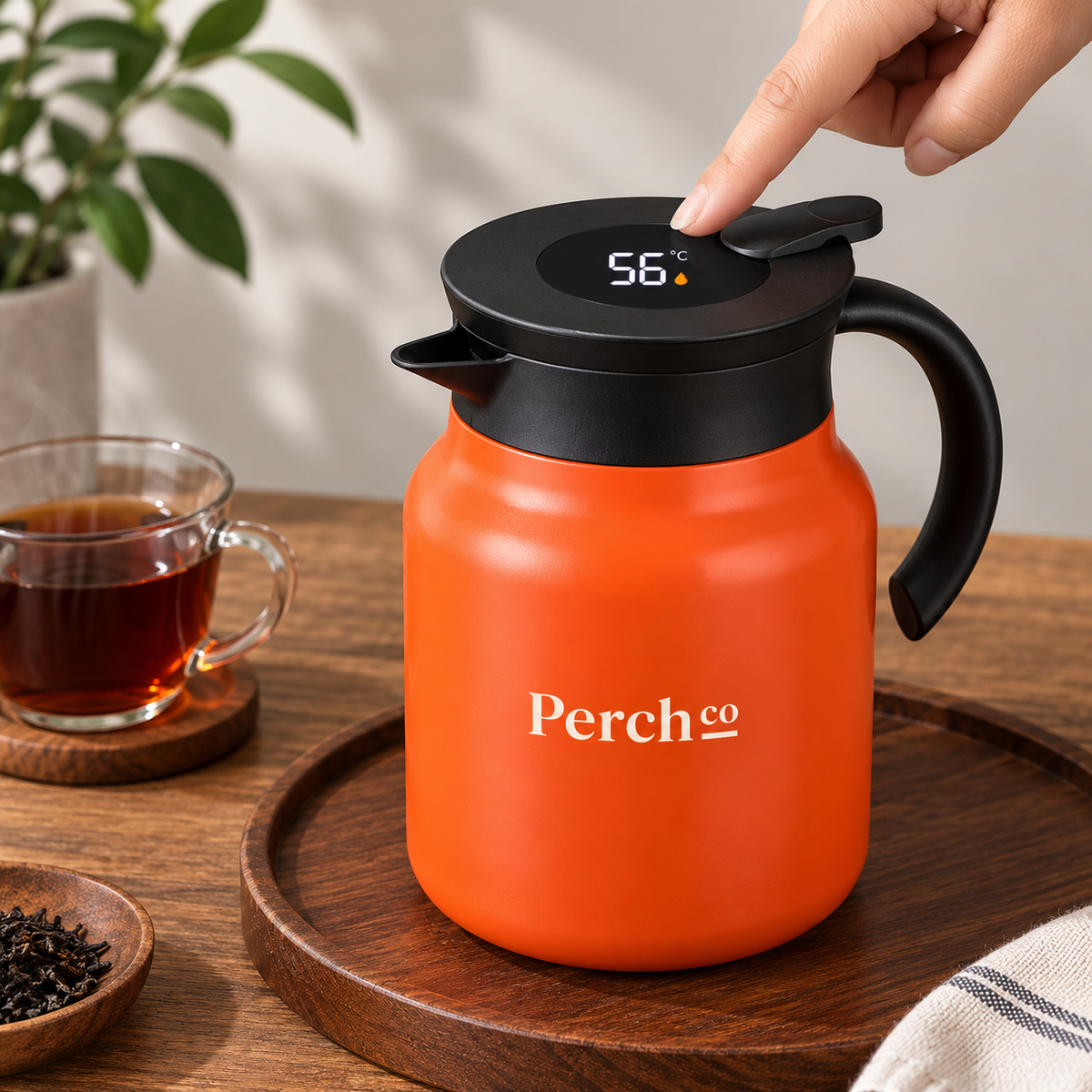 Perch Co branded insulated tea pot in orange with a finger touching the lid to wake the temperature display