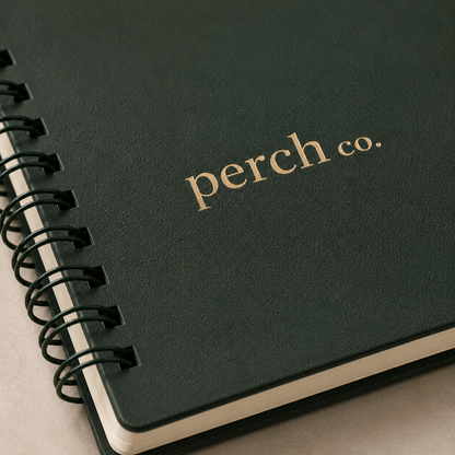 Close-up of the gold logo and twin-wire spiral on a dark green notebook